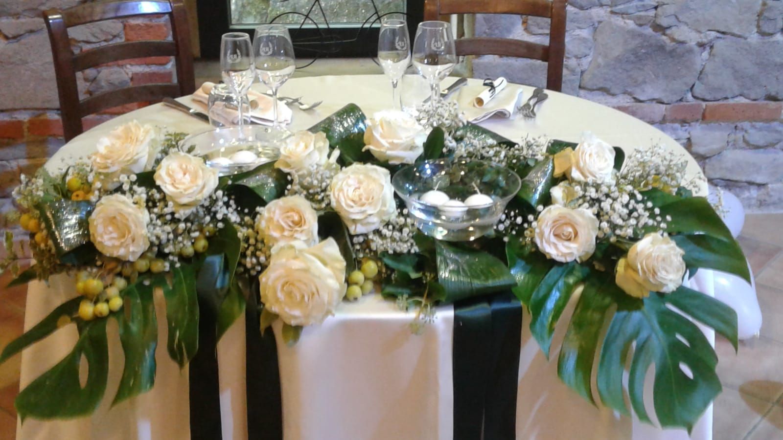 Tavolo apparecchiato per un matrimonio con rose color crema, verde e una ciotola di vetro centrale.