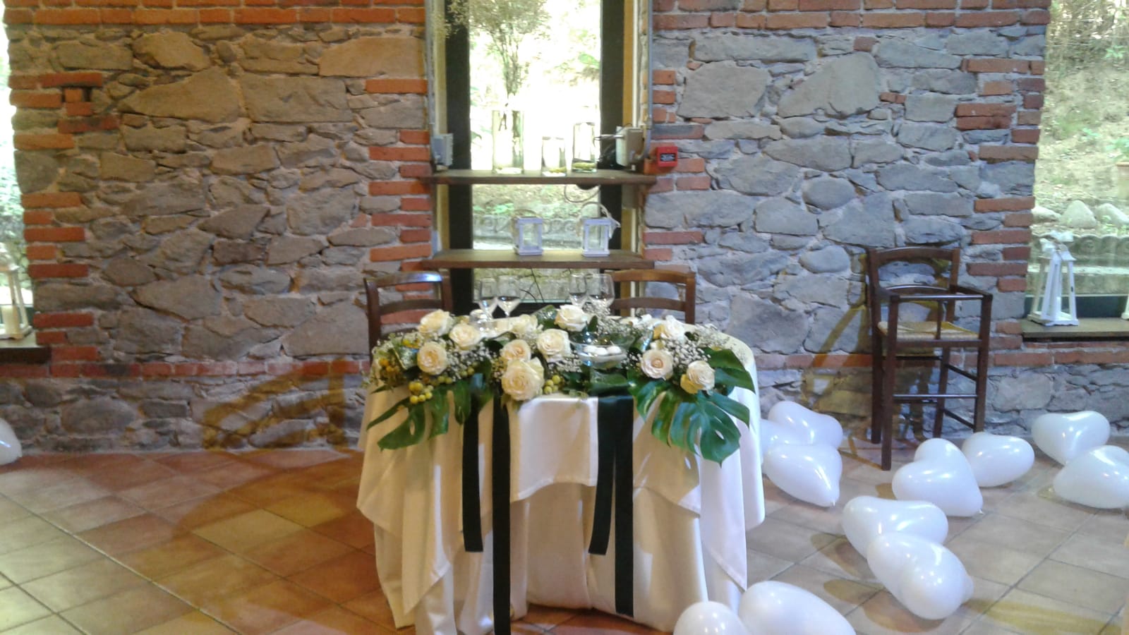 Tavolo nuziale con fiori bianchi e raso, palloncini, pareti in mattoni e pietra.