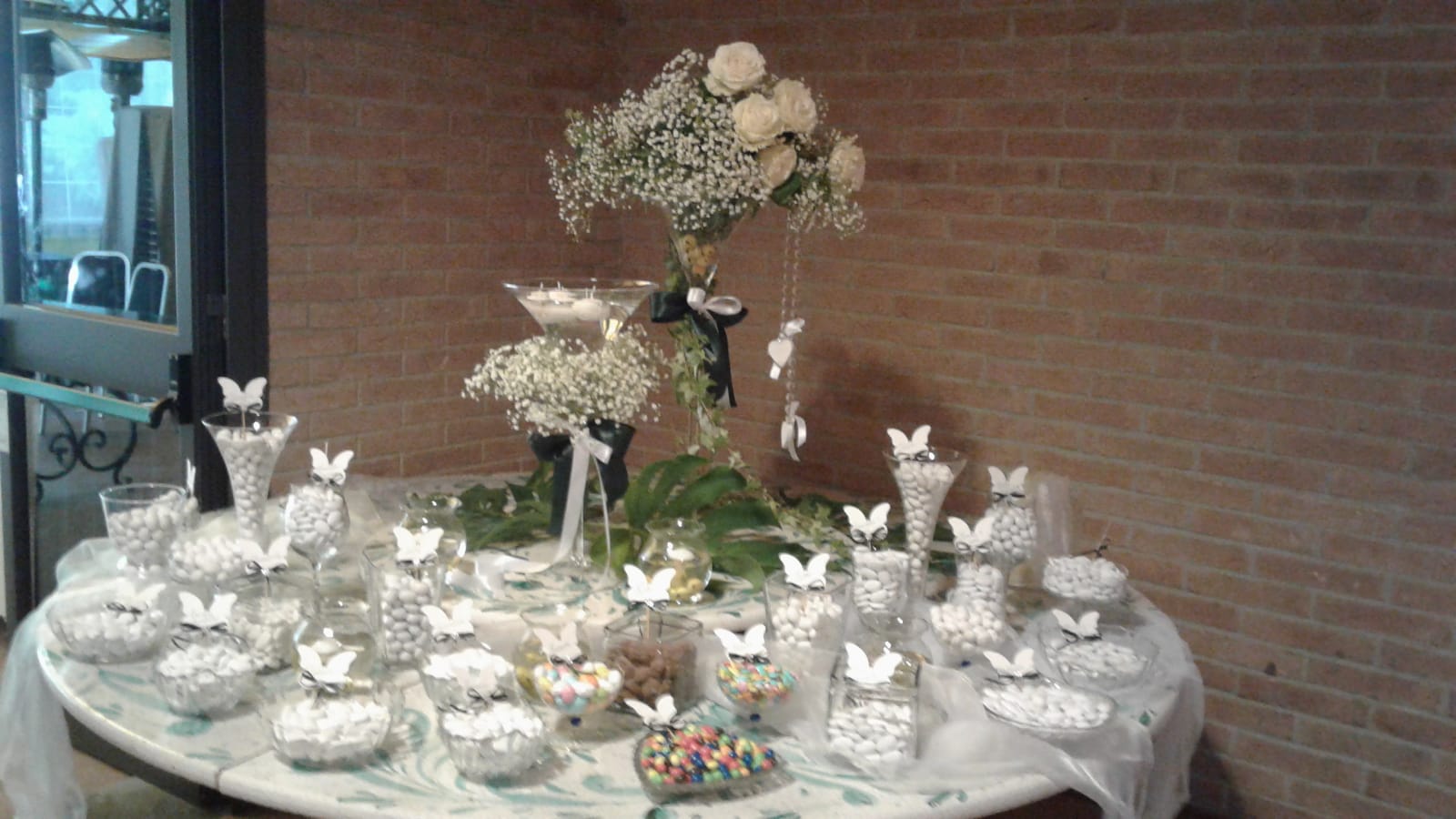 Buffet di dolciumi per matrimonio con rose bianche, gypsophila e decorazioni a farfalla.