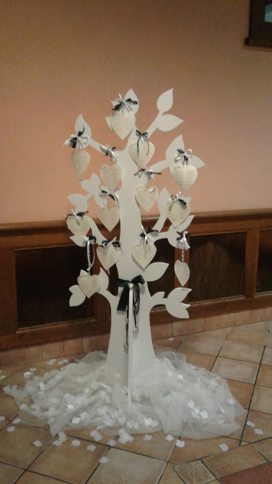 Albero decorativo bianco con cuori di carta e fiocchi, appoggiato su tulle e petali.