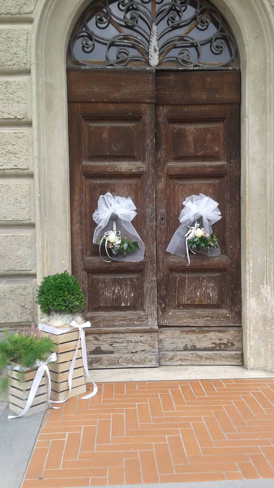 Doppie porte in legno decorate con fiocchi bianchi e composizioni floreali.