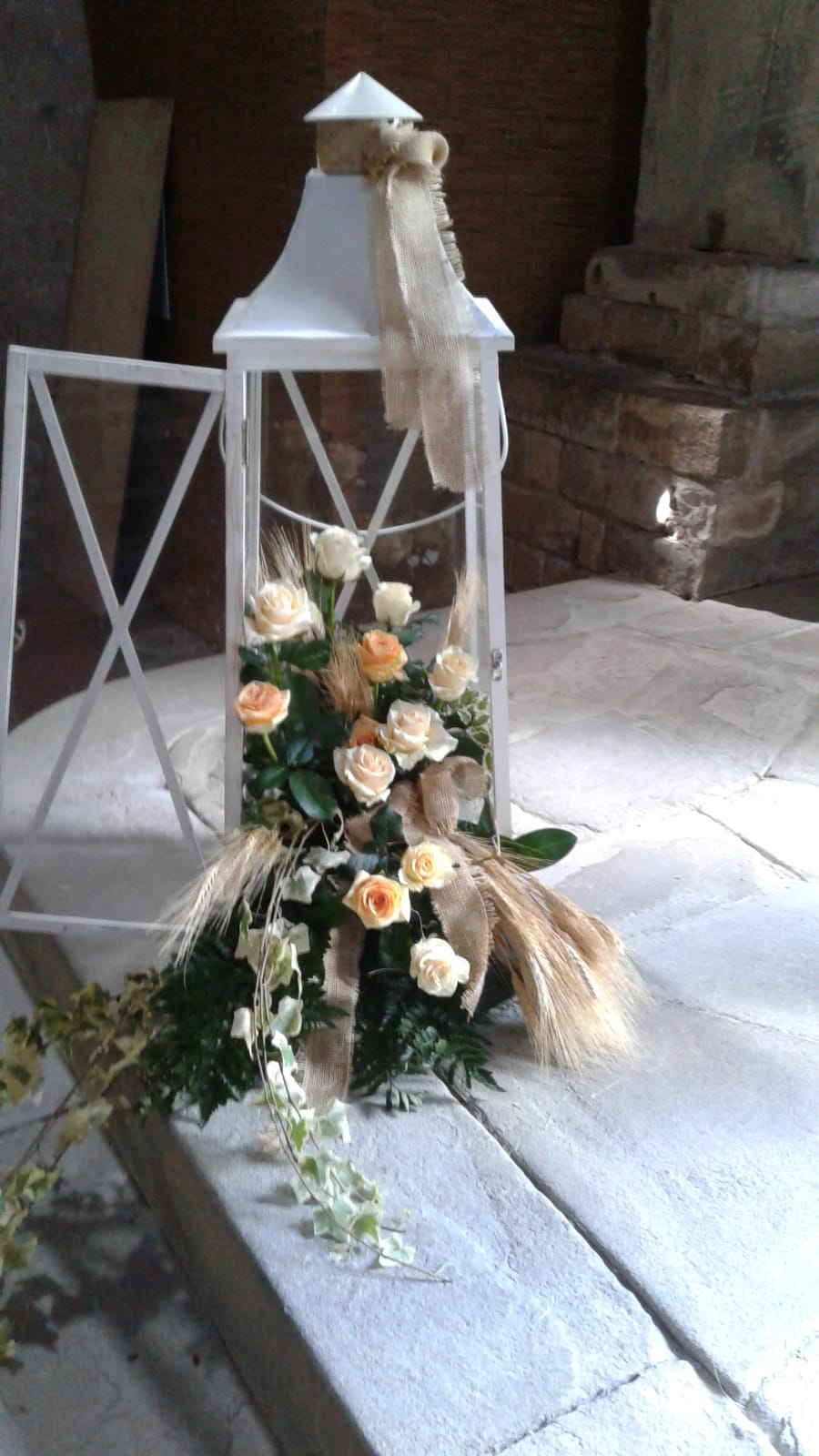 Lanterna bianca con composizione floreale, tra cui rose e verde, su una superficie di legno invecchiato.