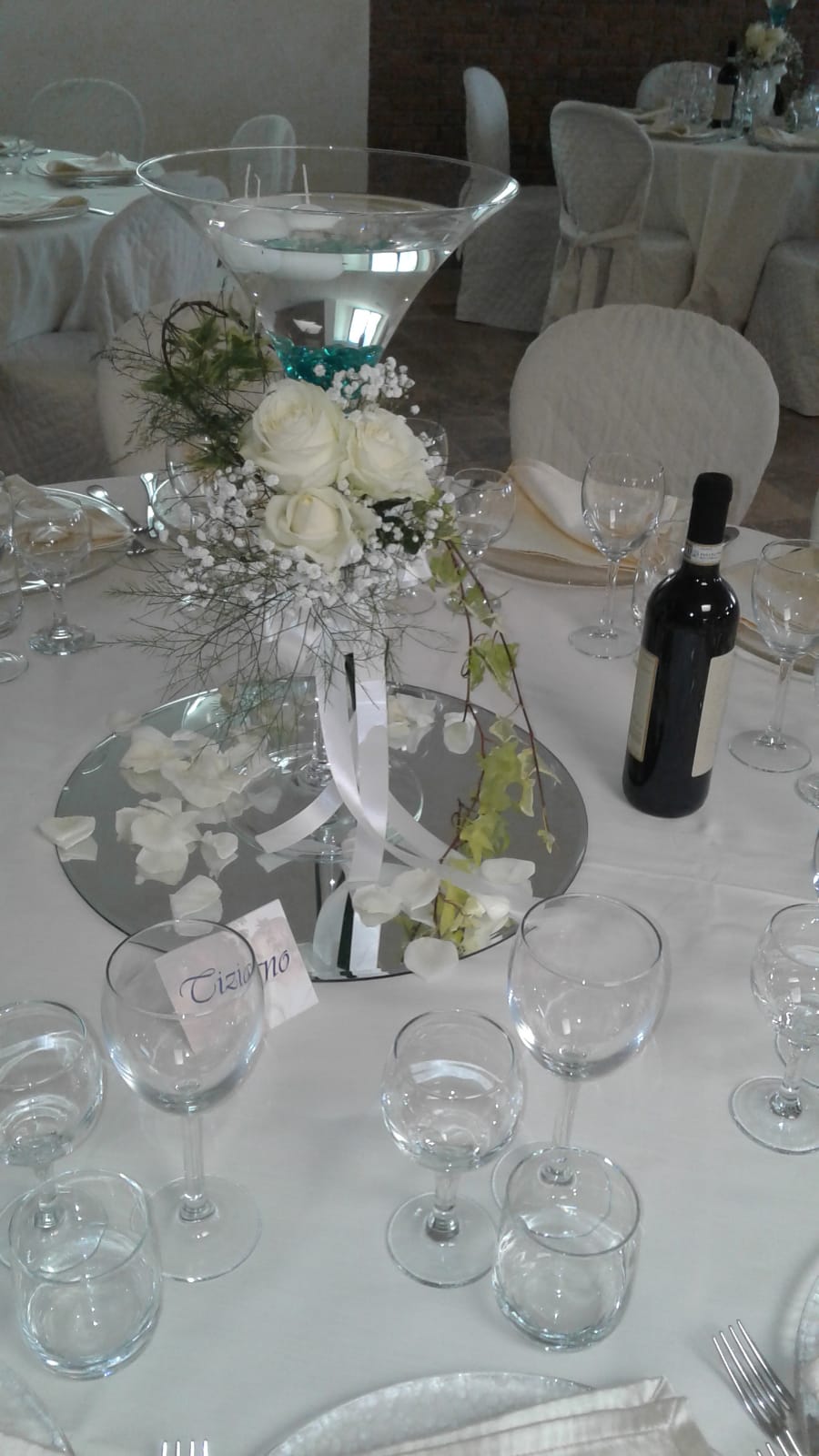 Apparecchiatura del tavolo nuziale con centrotavola floreale, bottiglia di vino e bicchieri.