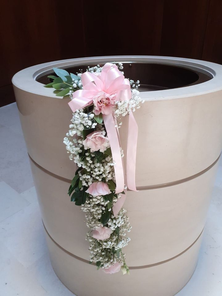 Fioriera cilindrica color marrone chiaro con una cascata di fiori rosa, gypsophila e un fiocco rosa.
