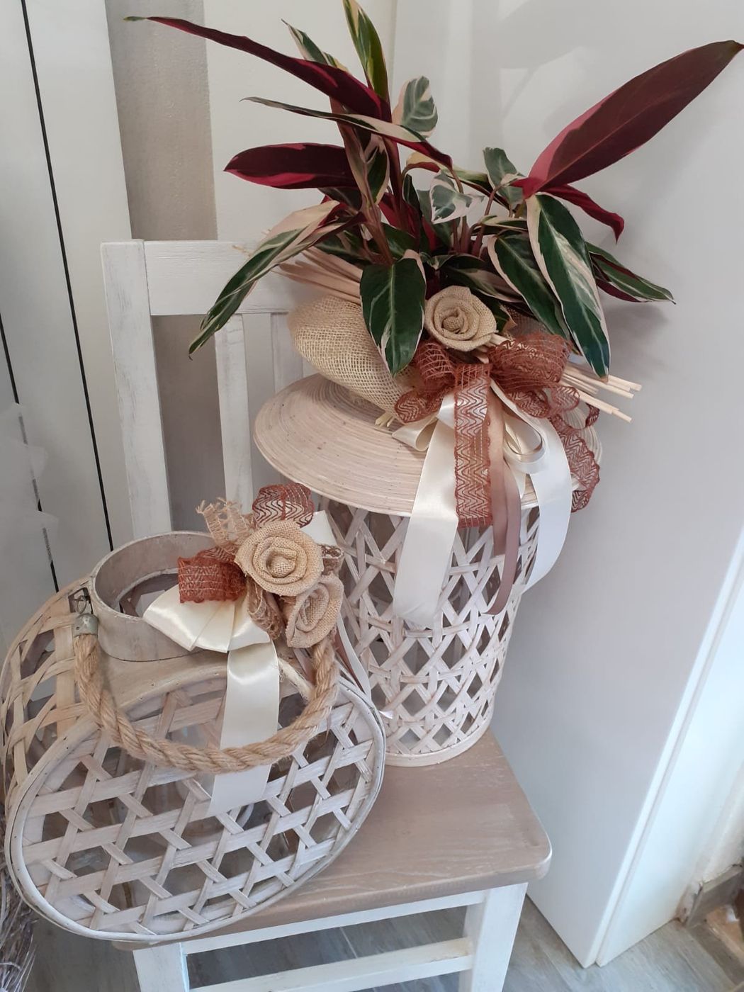 Due cestini decorativi in vimini, uno con piante e nastro, su una sedia bianca.