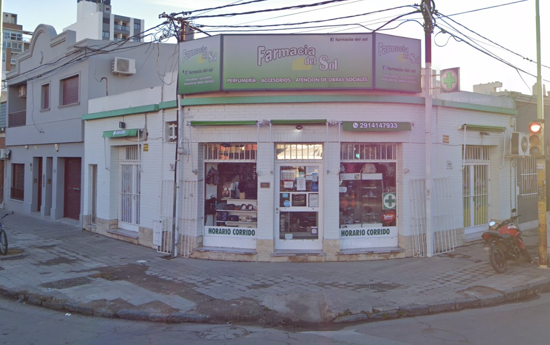 Local comercial en esquina con fachada blanca, letrero verde y puertas de cristal en una calle al anochecer.