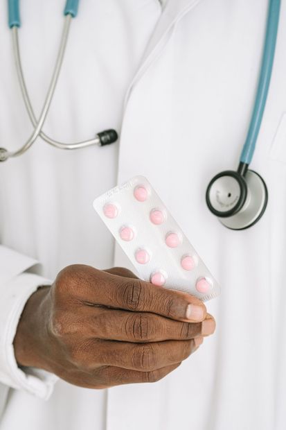 Médico sosteniendo un blíster de pastillas rosas, con el estetoscopio visible.