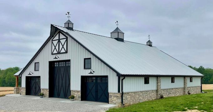 A large white barn with black doors is sitting in the middle of a grassy field. A large white barn with black doors is sitting in the middle of a grassy field.
