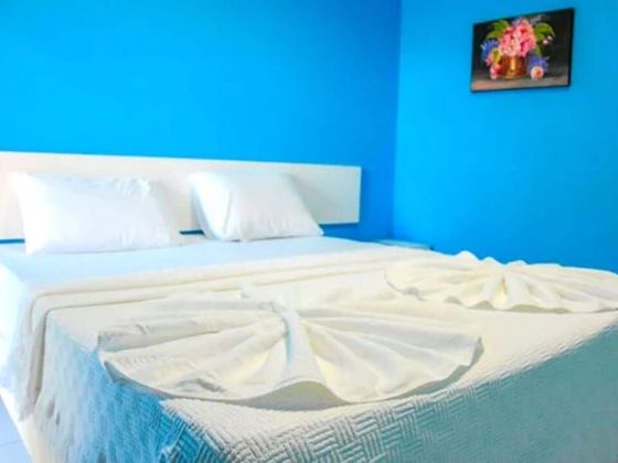 Quarto de hotel com decoração em tons de branco e bege, duas camas, uma pequena TV e uma varanda com vegetação.