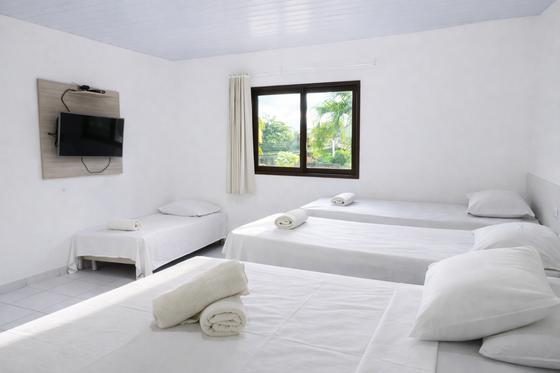 Quarto com três camas, um espelho e uma varanda com decoração em tons de verde vibrante.