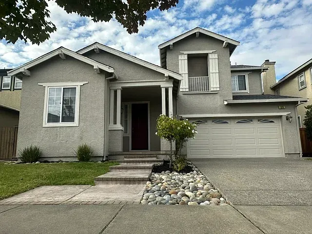 Gray suburban house with two-car garage, front steps, and landscaped yard under a cloudy sky
