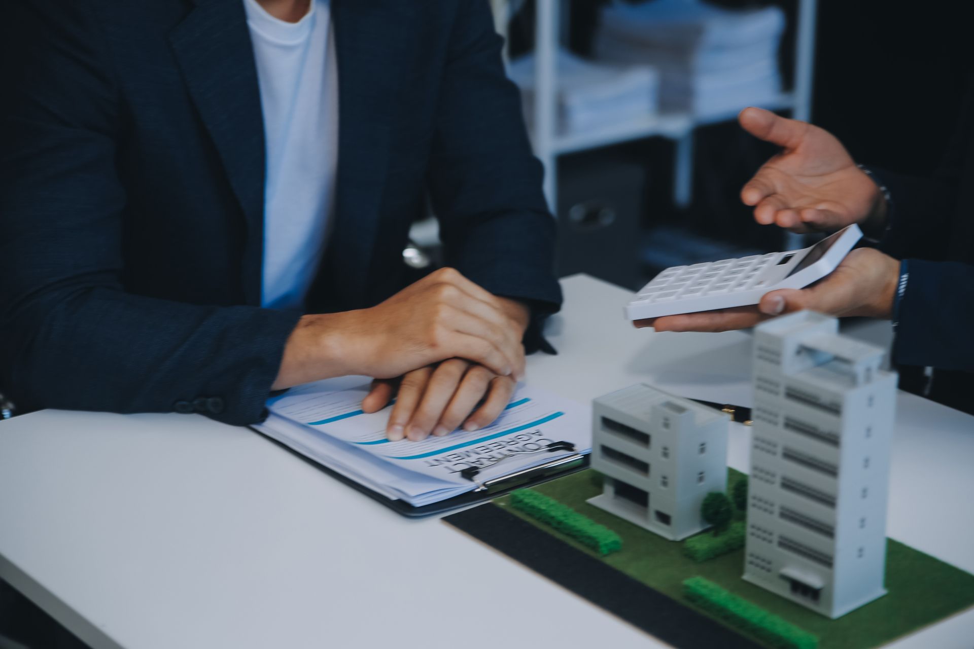 Two people at a desk with an architectural model of buildings, discussing real estate or property investment.