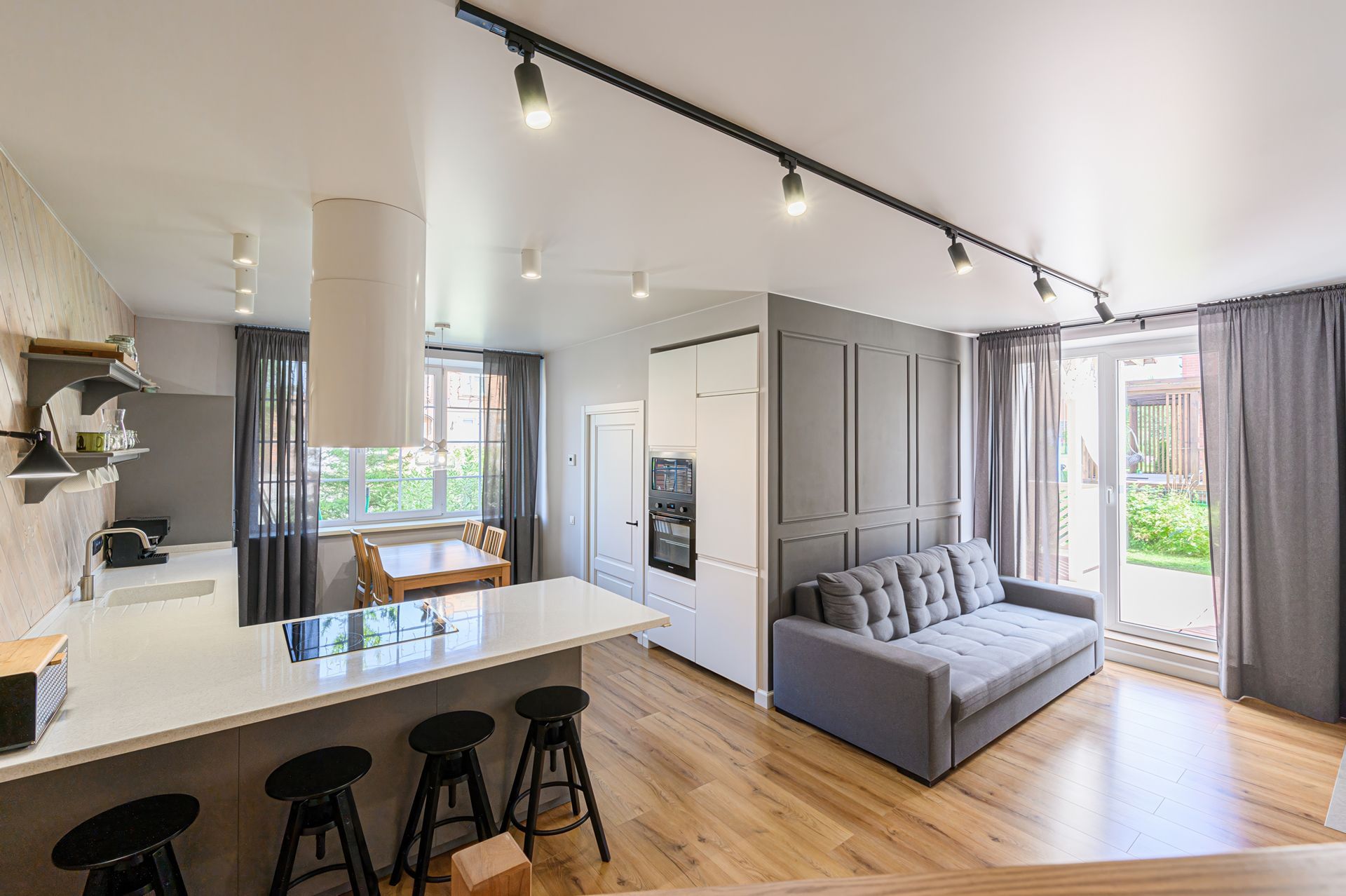 A bright, modern open-plan apartment featuring a kitchen with a white island, a dining area, and a grey sofa.