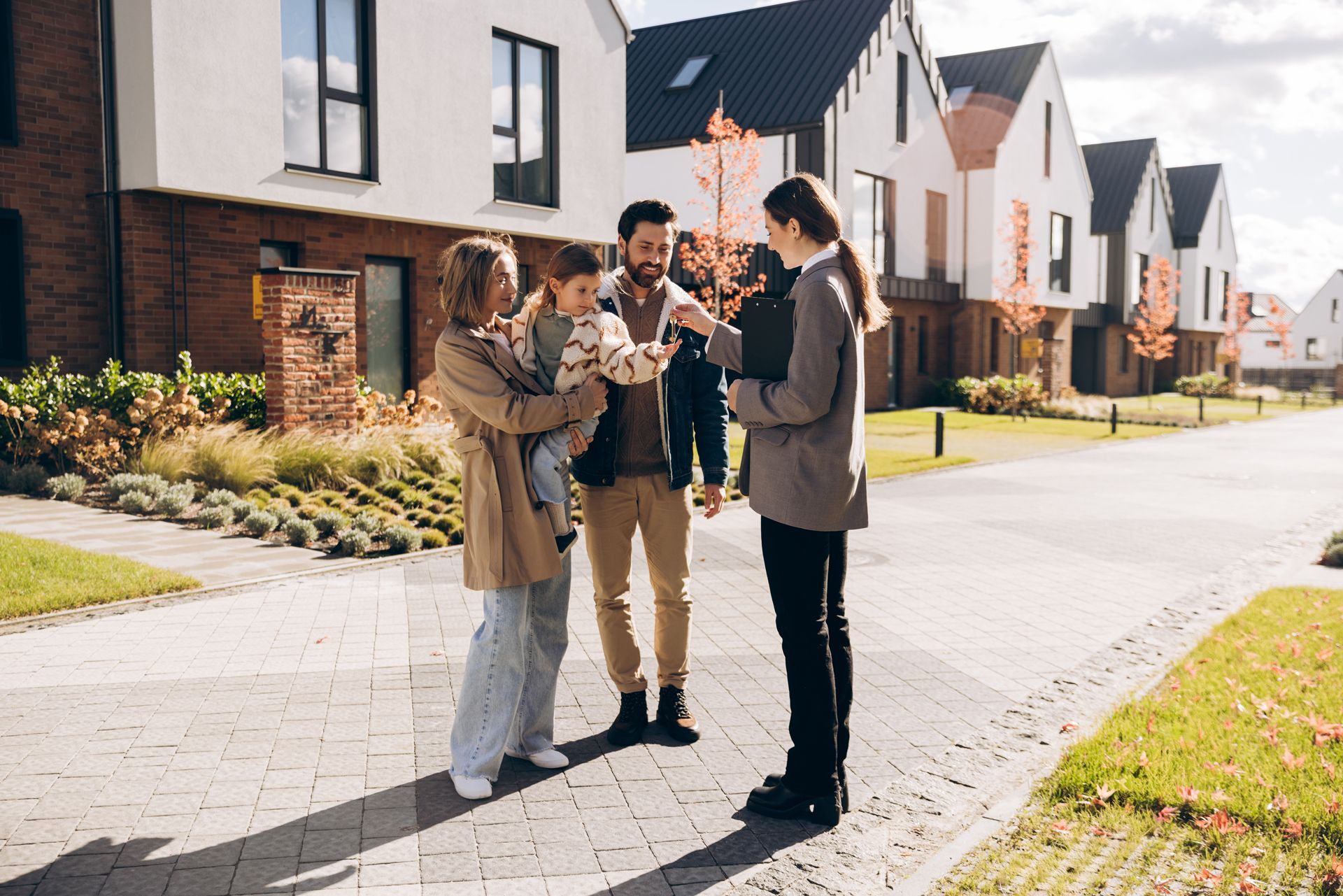 A real estate agent talks to a family outside a row of modern houses on a sunny day.
