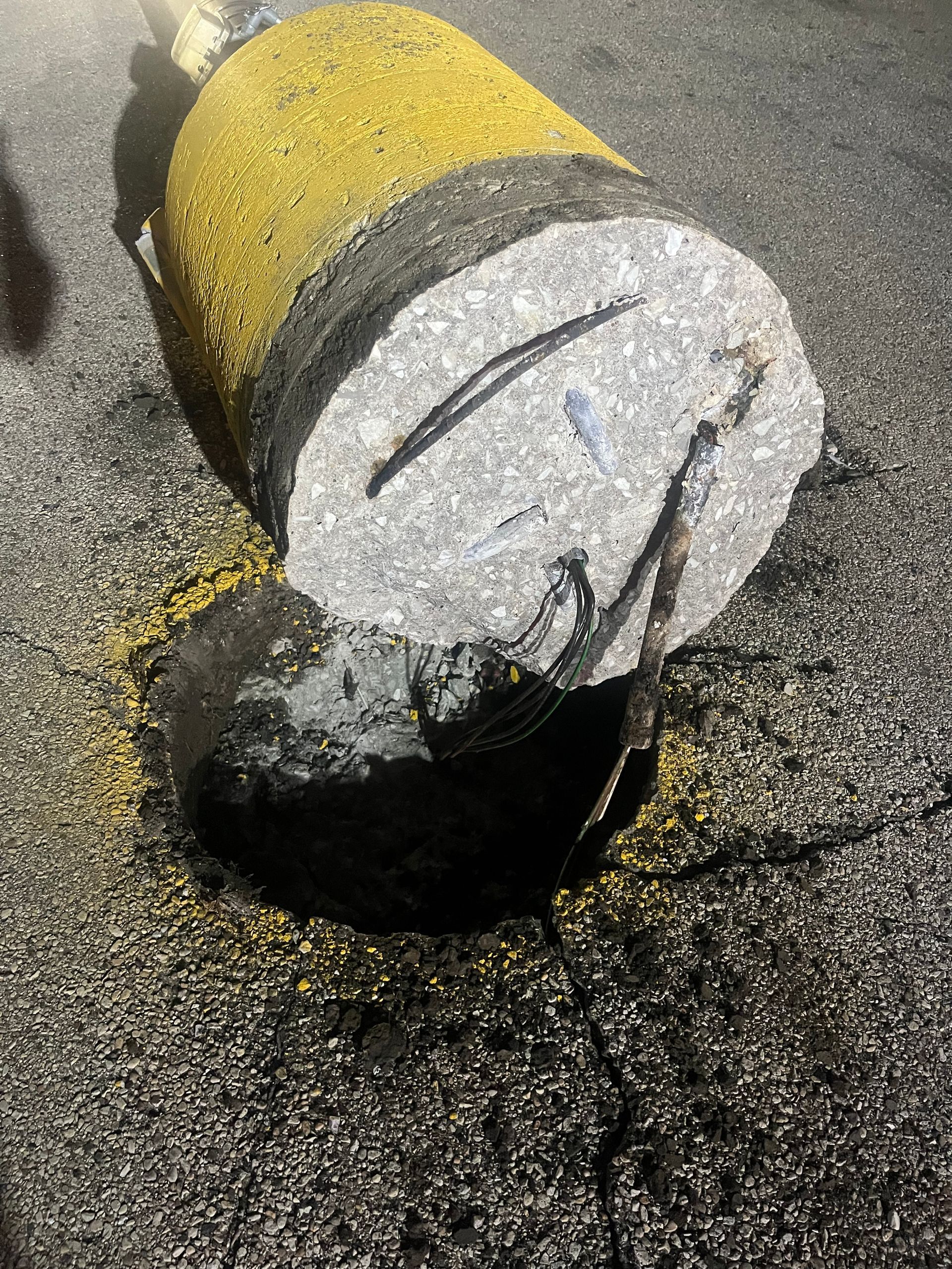 Yellow and black cylindrical road marker lying in a dark asphalt hole.