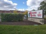 Sign for Bowser's Pizza in front of a building, green bushes, and cloudy sky.