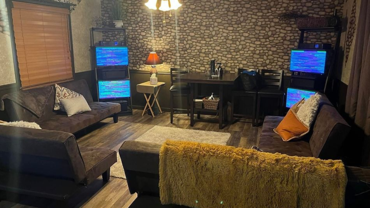 Living room with dark furniture, stone accent wall, and multiple monitors displaying static.