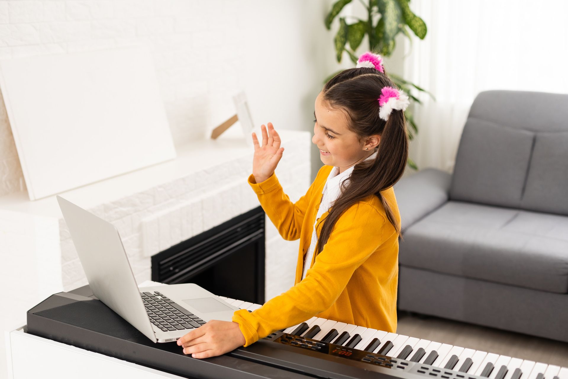 Girl playing keyboard in a bright living room with a laptop open nearby
