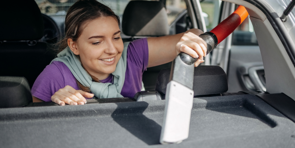 A woman is cleaning the trunk of a car with a vacuum cleaner.
