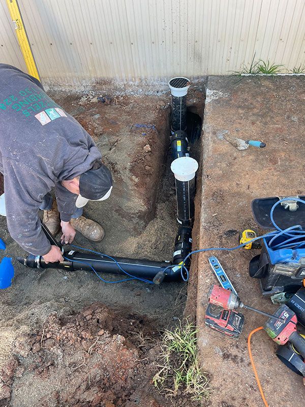 A Man Is Working On A Pipe In The Dirt — Pertzels Plumbing In Wagga Wagga, NSW
