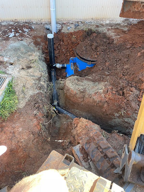 A Man Is Digging A Hole In The Ground To Install A Pipe — Pertzels Plumbing In Wagga Wagga, NSW
