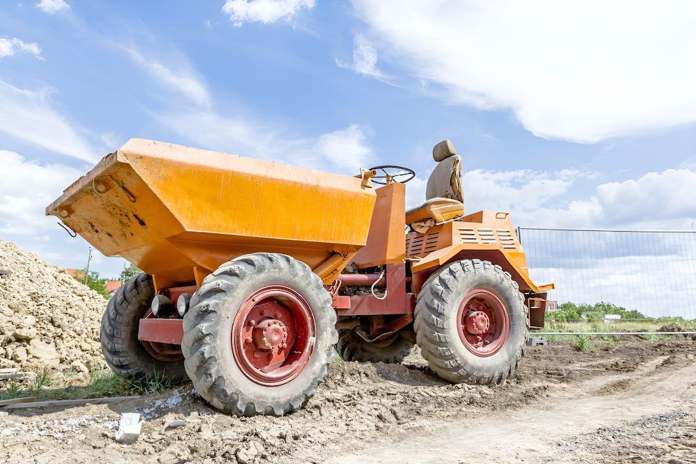 A Man Is Driving A Dump Truck On A Dirt Road — Wilsons Excavations & Plant Hire in Ballina, NSW