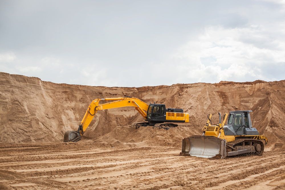 A Bulldozer And An Excavator Are Working In A Dirt Pit — Wilsons Excavations & Plant Hire in Bangalow, NSW