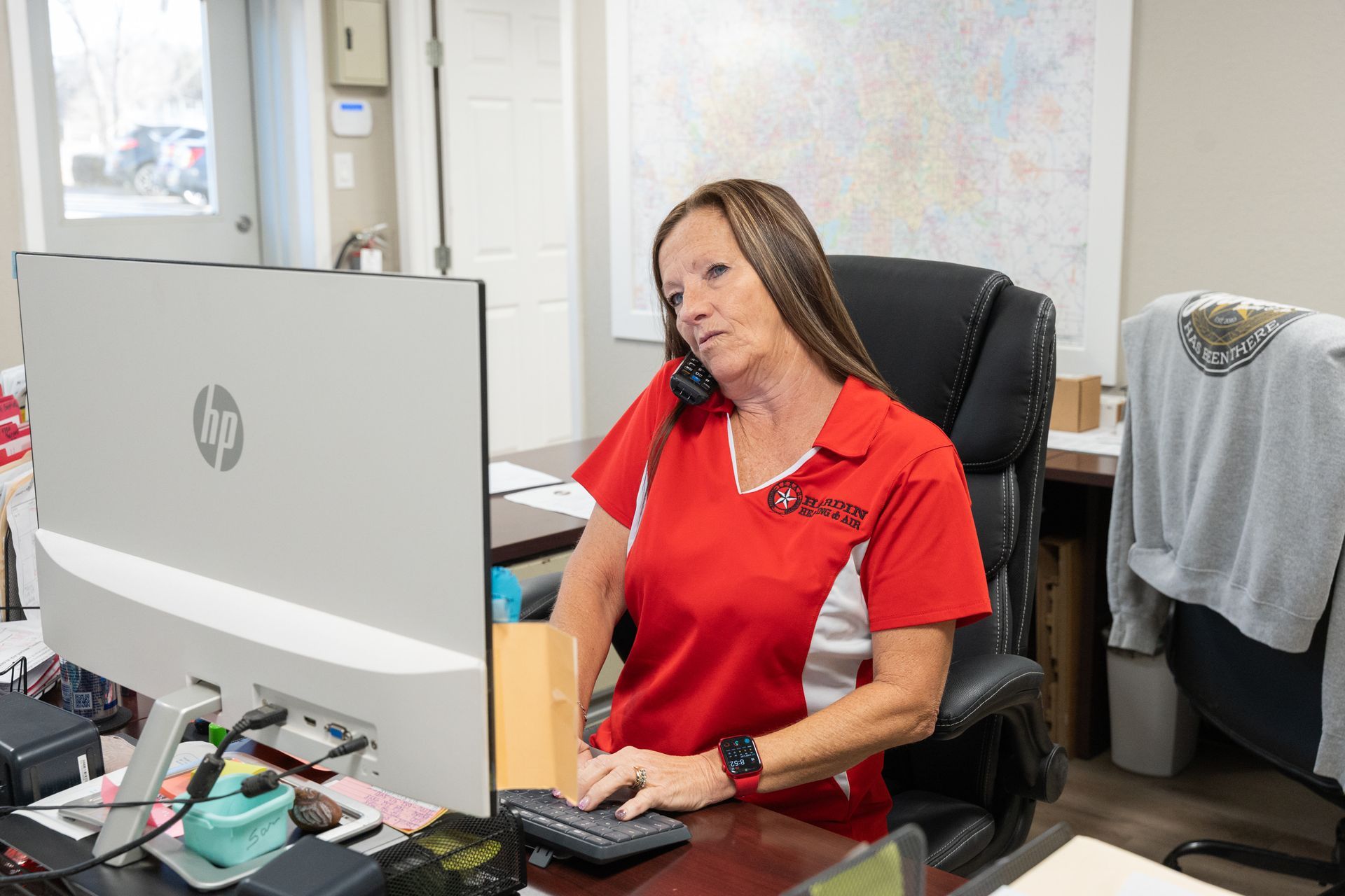 Woman in red shirt on phone, typing at a computer in an office.