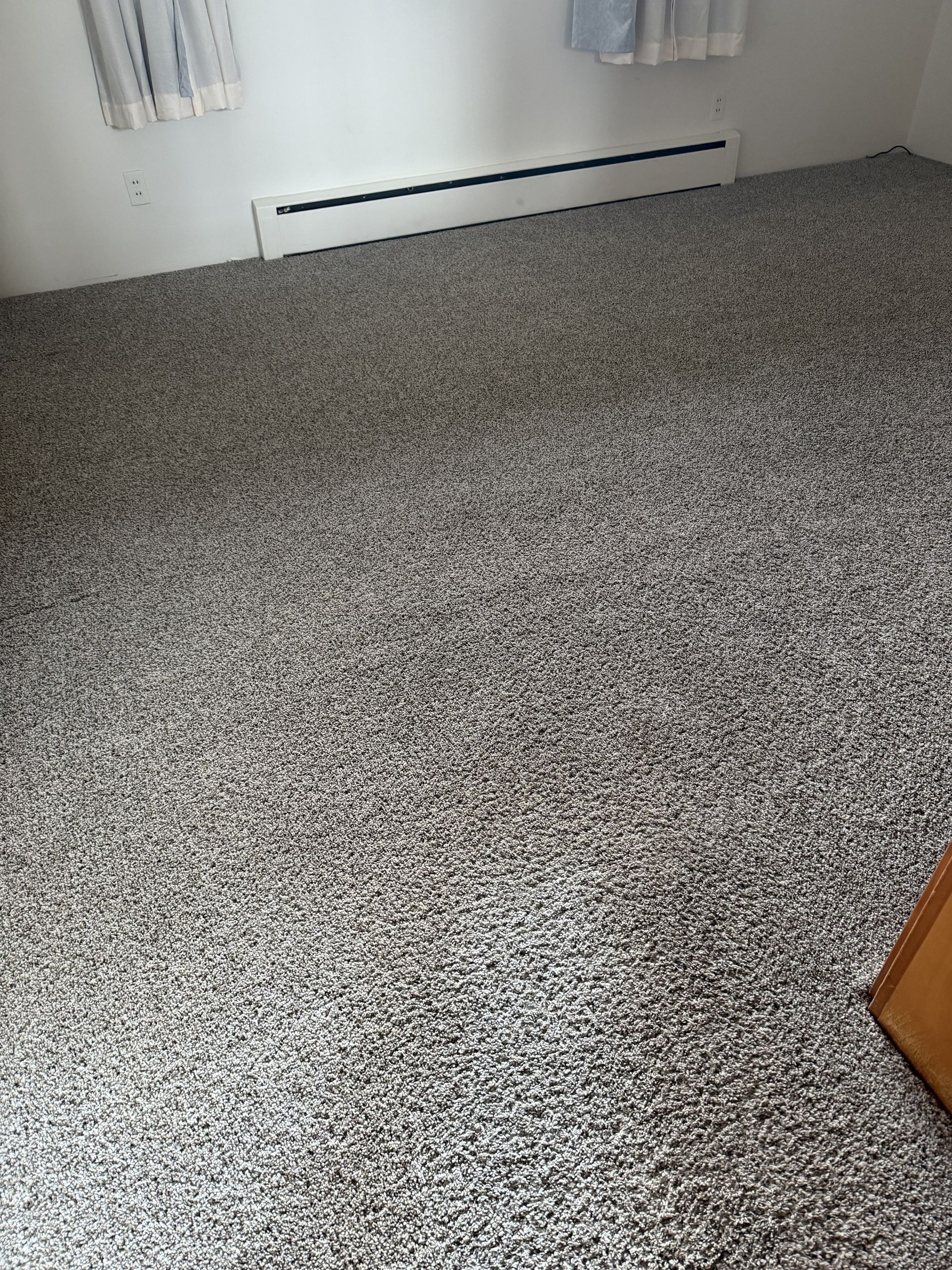 Small room with speckled carpet, white walls, baseboard heater, and a wooden cabinet edge.