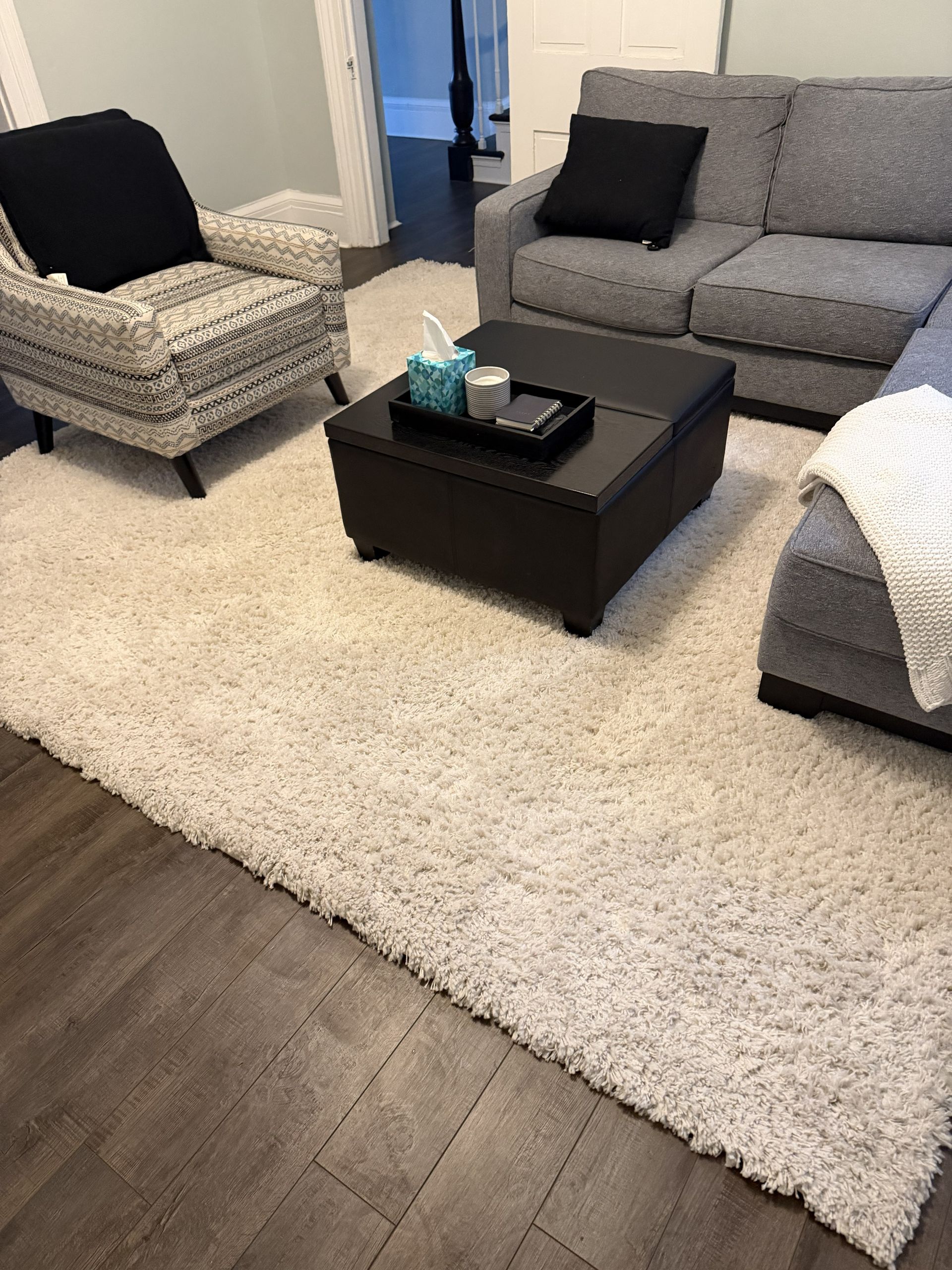 Living room with gray furniture, black coffee table, and large white shag rug on dark wood floor
