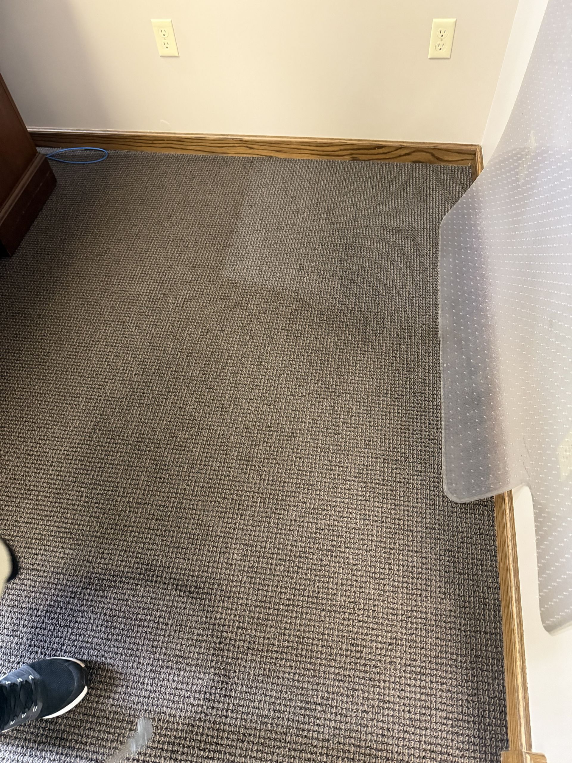 Carpeted floor with a patterned rug, wall outlets, and a partial curtain in a corner room.