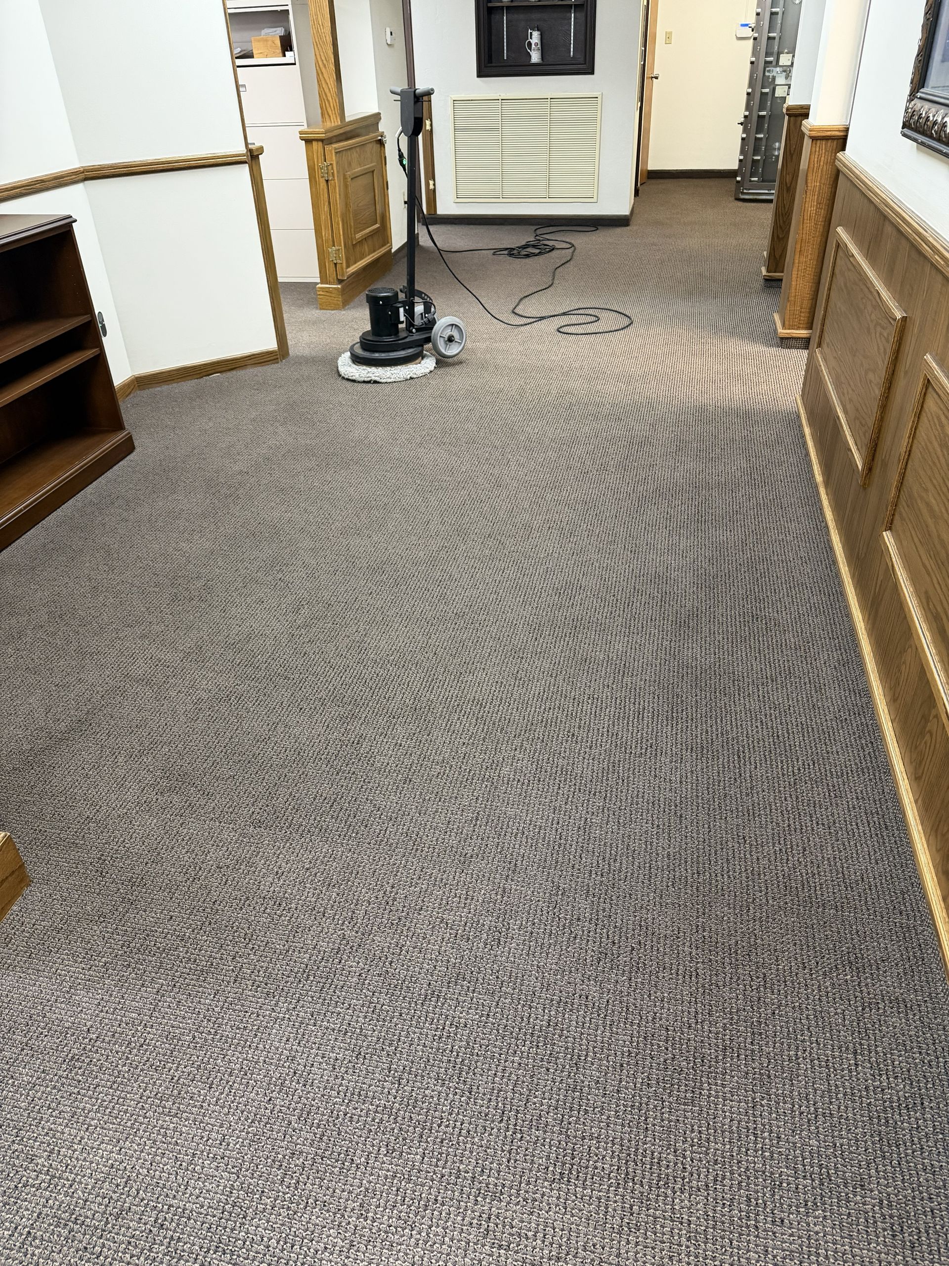 Carpeted hallway with a carpet cleaner centered near a white appliance and wood paneling.