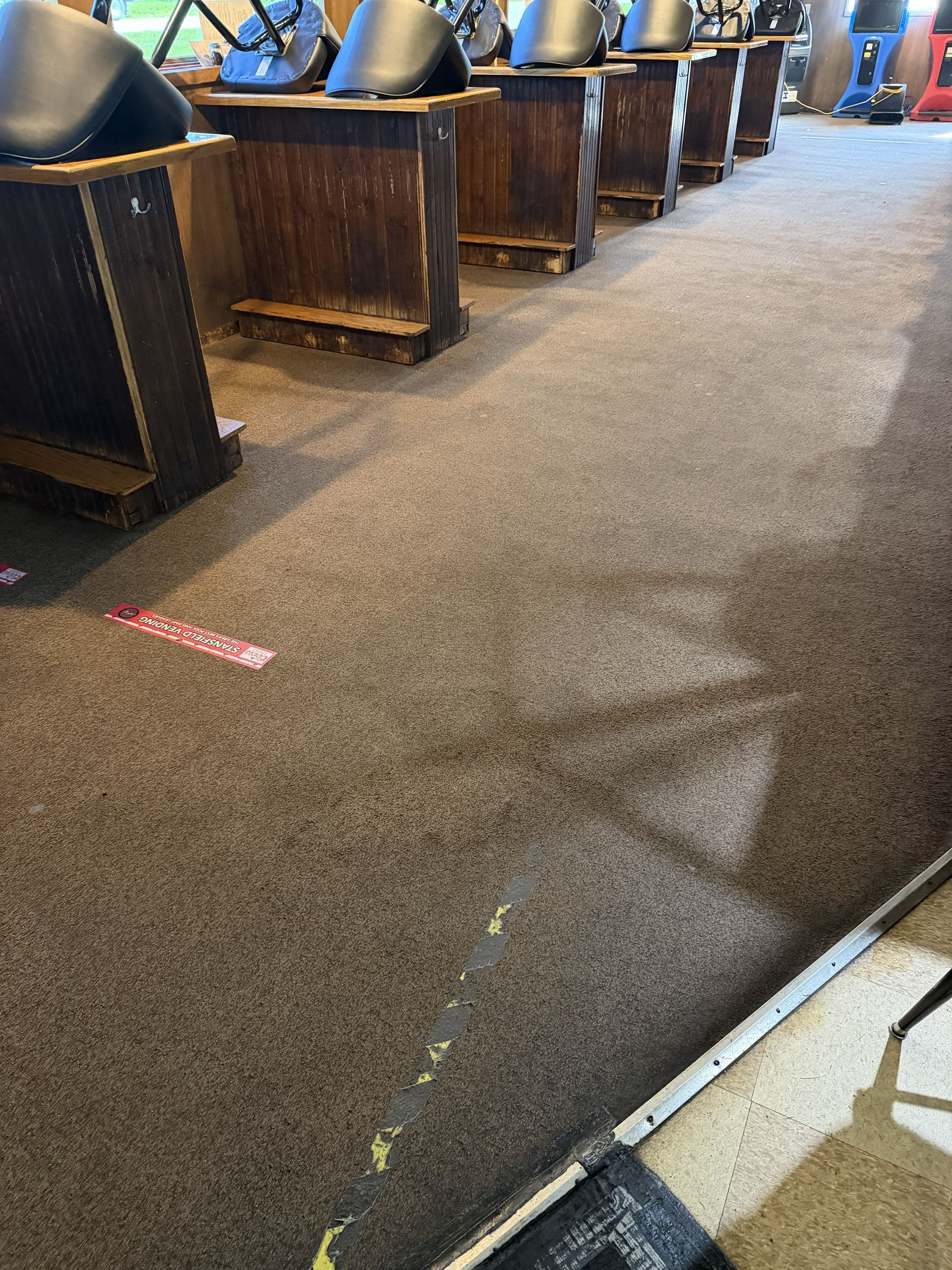 Carpeted arcade with row of bowling lanes and ball returns under bright overhead lights