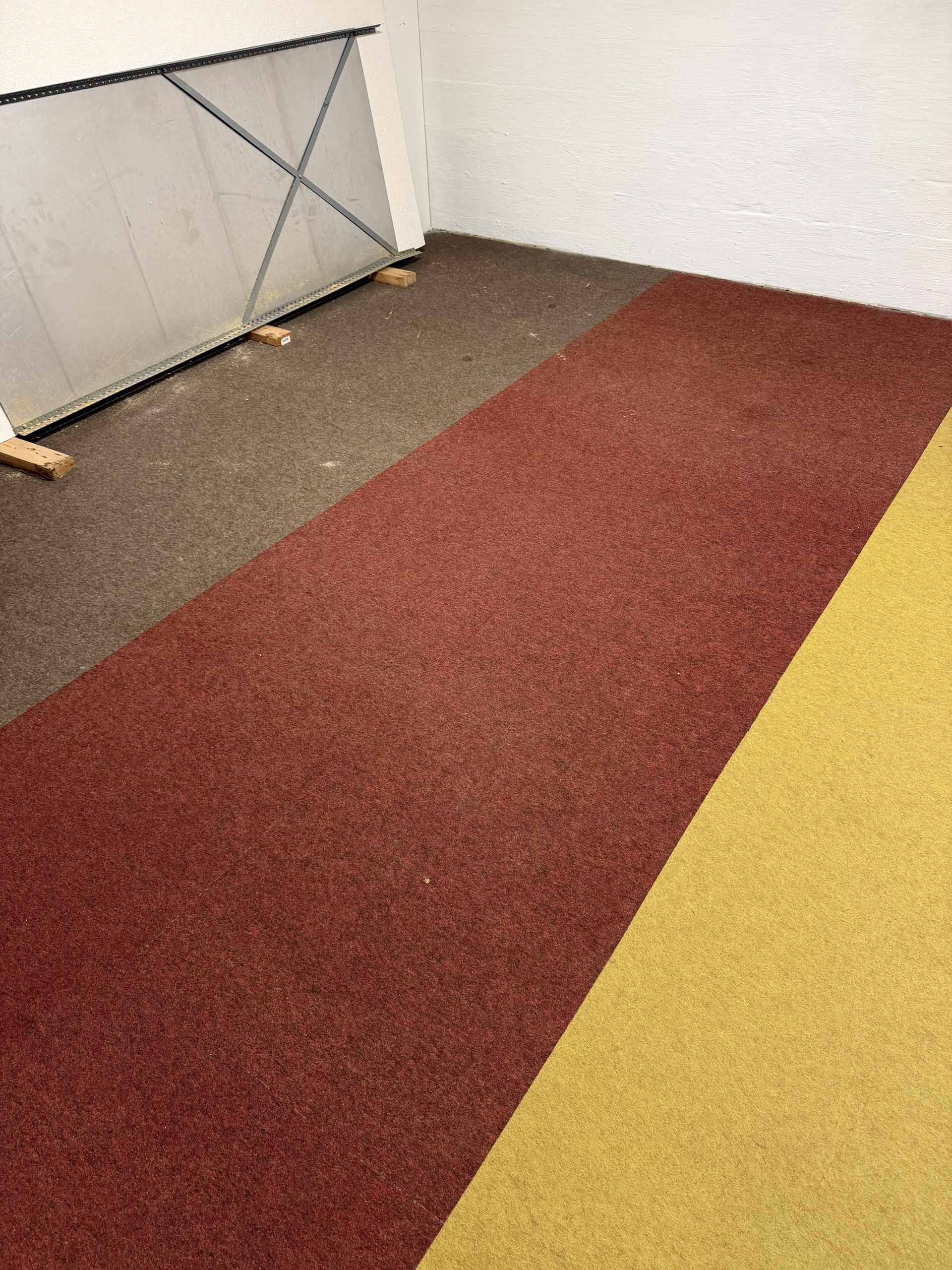 Indoor hallway with red carpet runner, yellow flooring edge, and a metal railing along the wall.