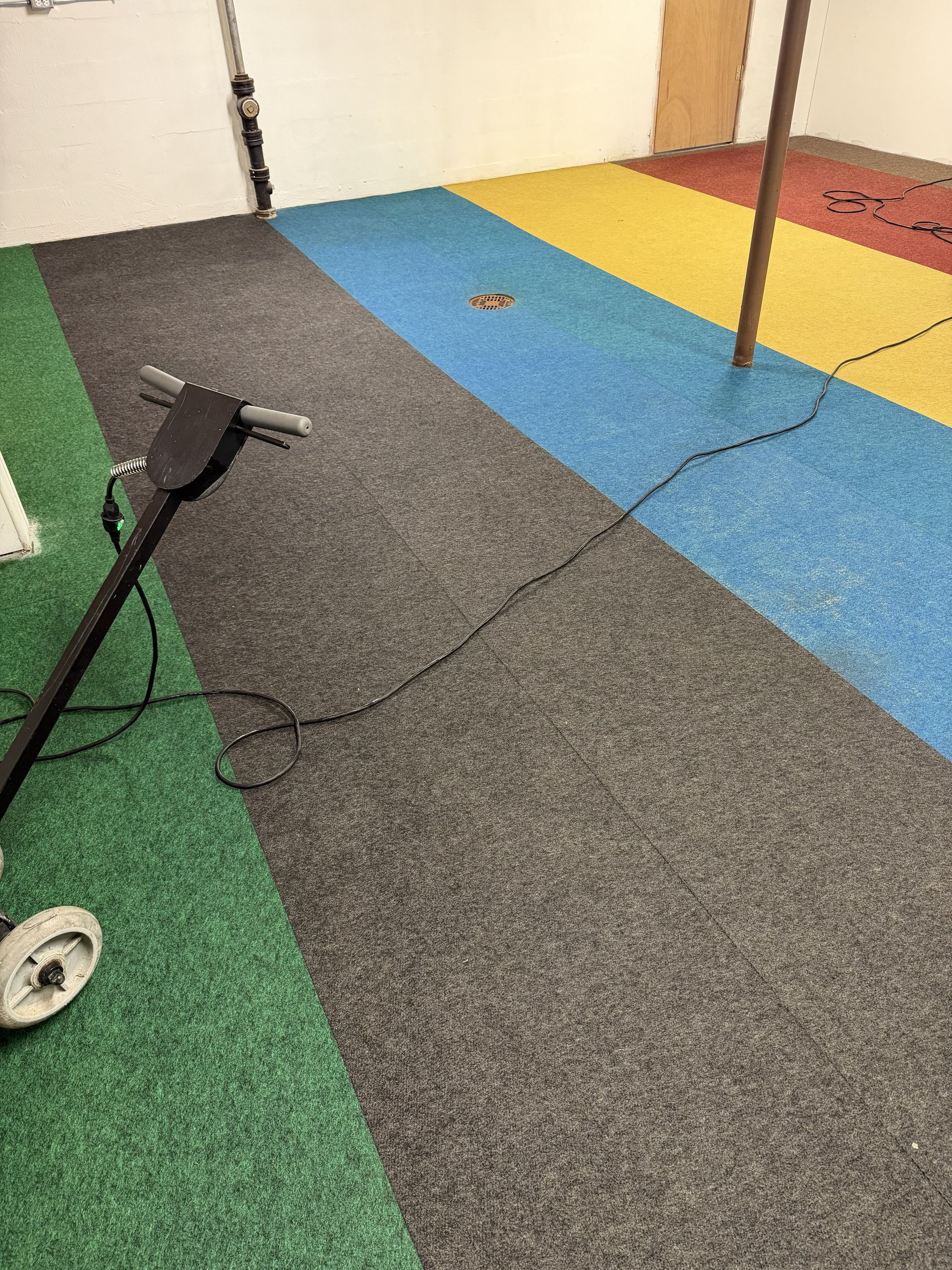 Indoor room with colorful carpet tiles, a cable, and exercise/pole equipment on the floor