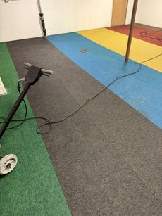 Indoor room with colorful carpet tiles, a cable, and exercise/pole equipment on the floor