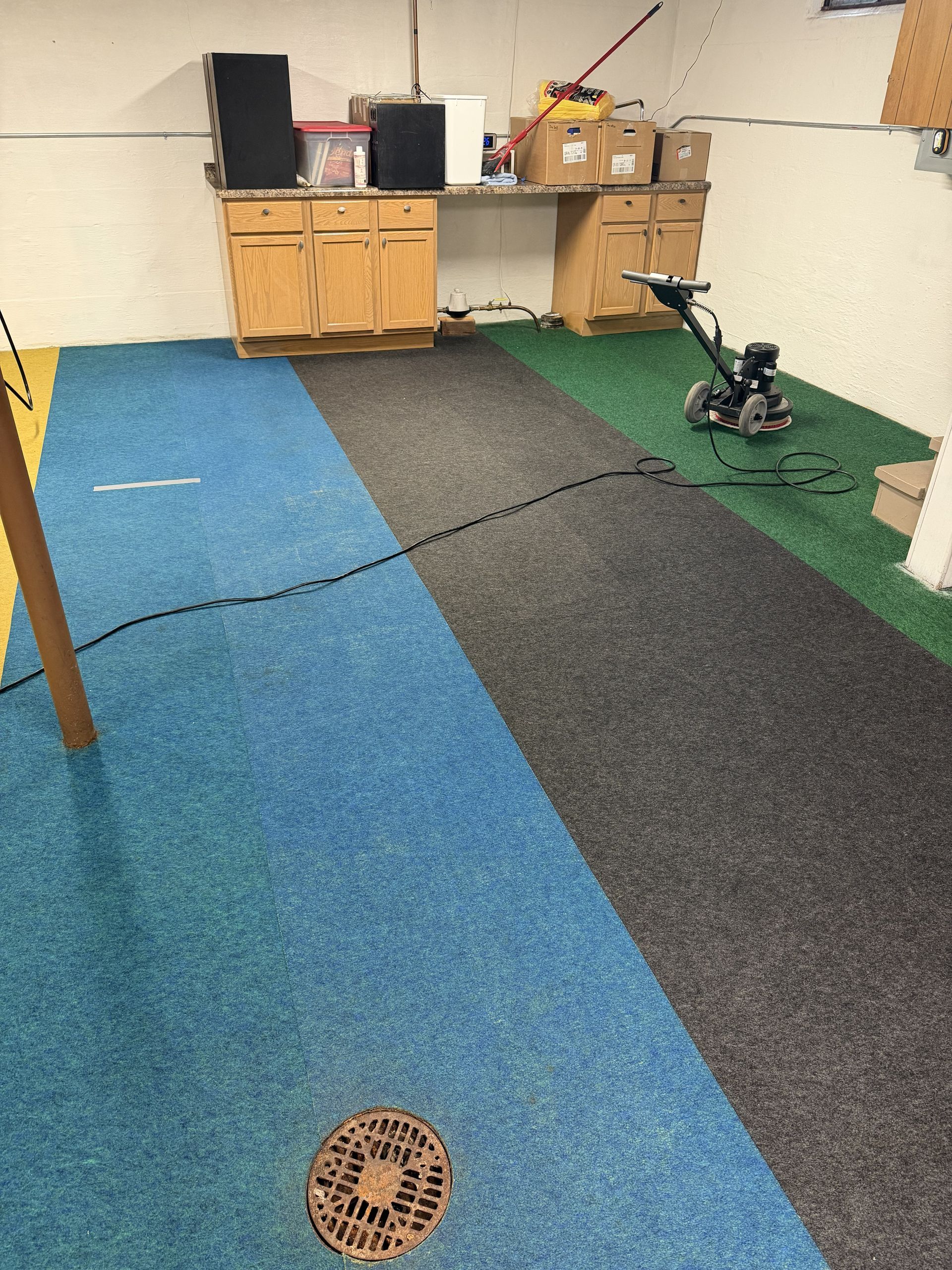 Basement room with blue and gray carpet tiles, cabinets, and a small exercise bike on a green mat.