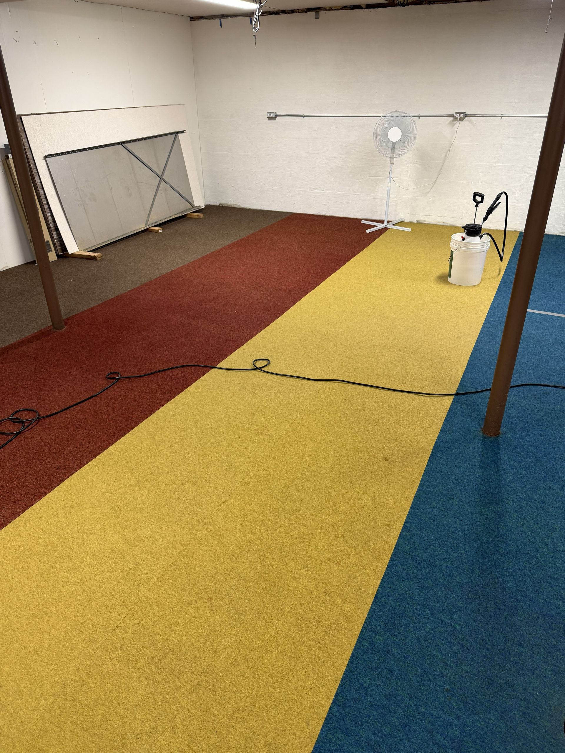 Indoor room with red, yellow, and blue carpet strips, a fan, and white walls.