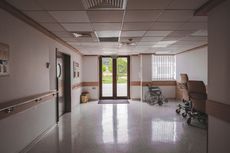Empty hospital hallway with wheelchairs, glossy floor, and glass doors at the end