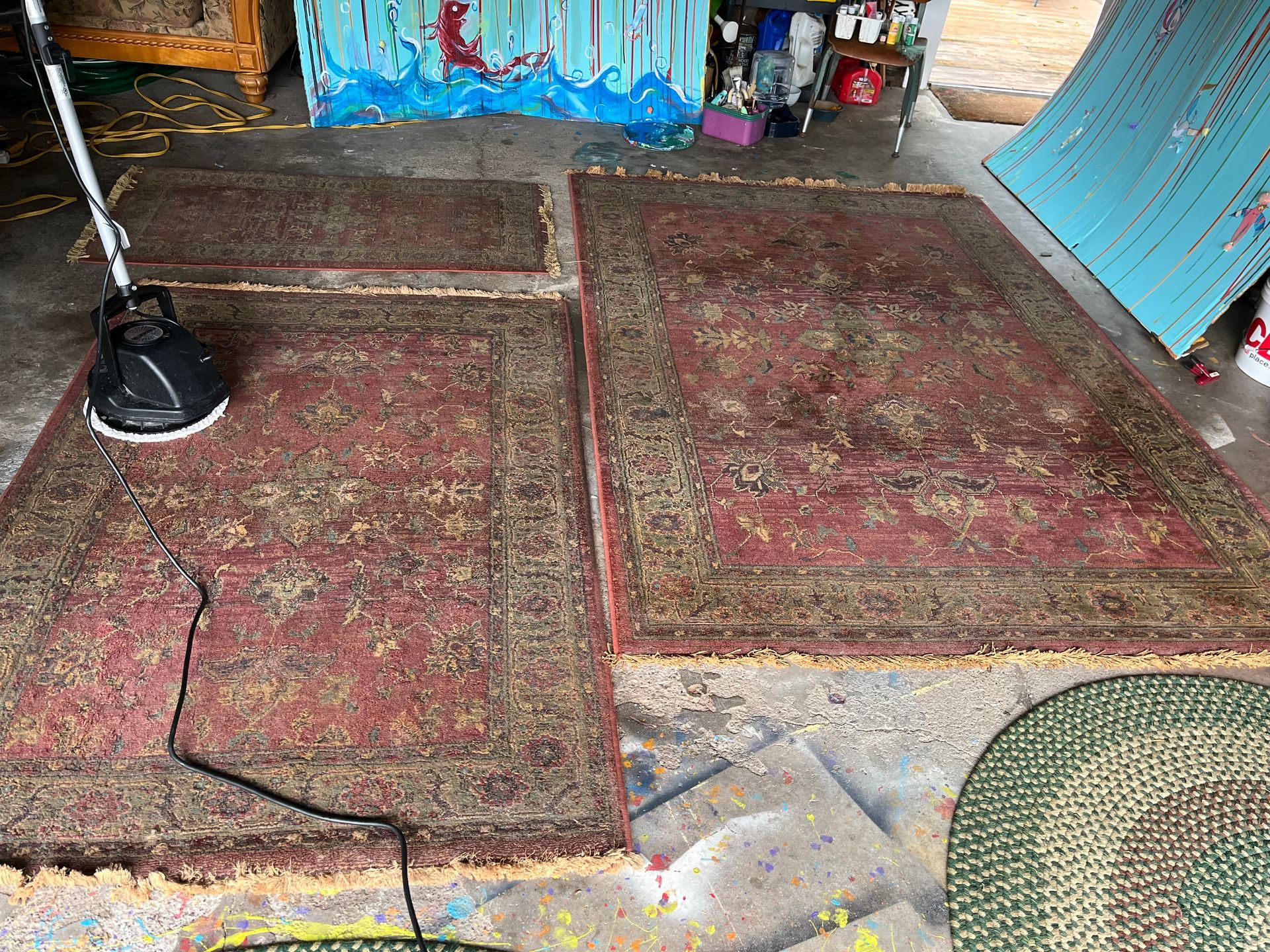 Two worn red rugs on a floor, with a black lamp and cable at left, beside blue painted doors.