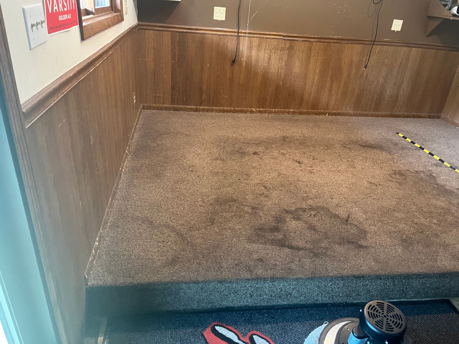 Empty carpeted room with wood-paneled walls and a small toy wheel at the bottom right.