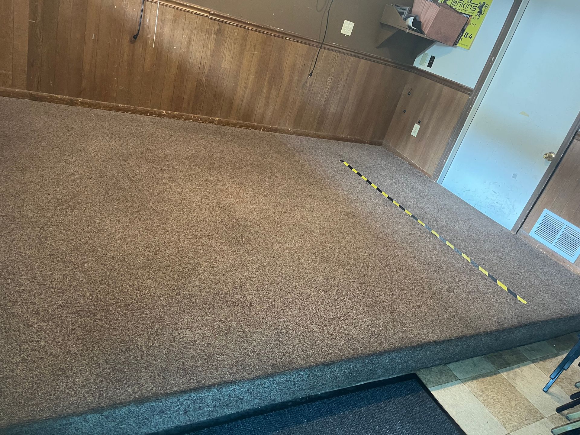 Empty carpeted room with wood-paneled walls and a light blue door on the right.