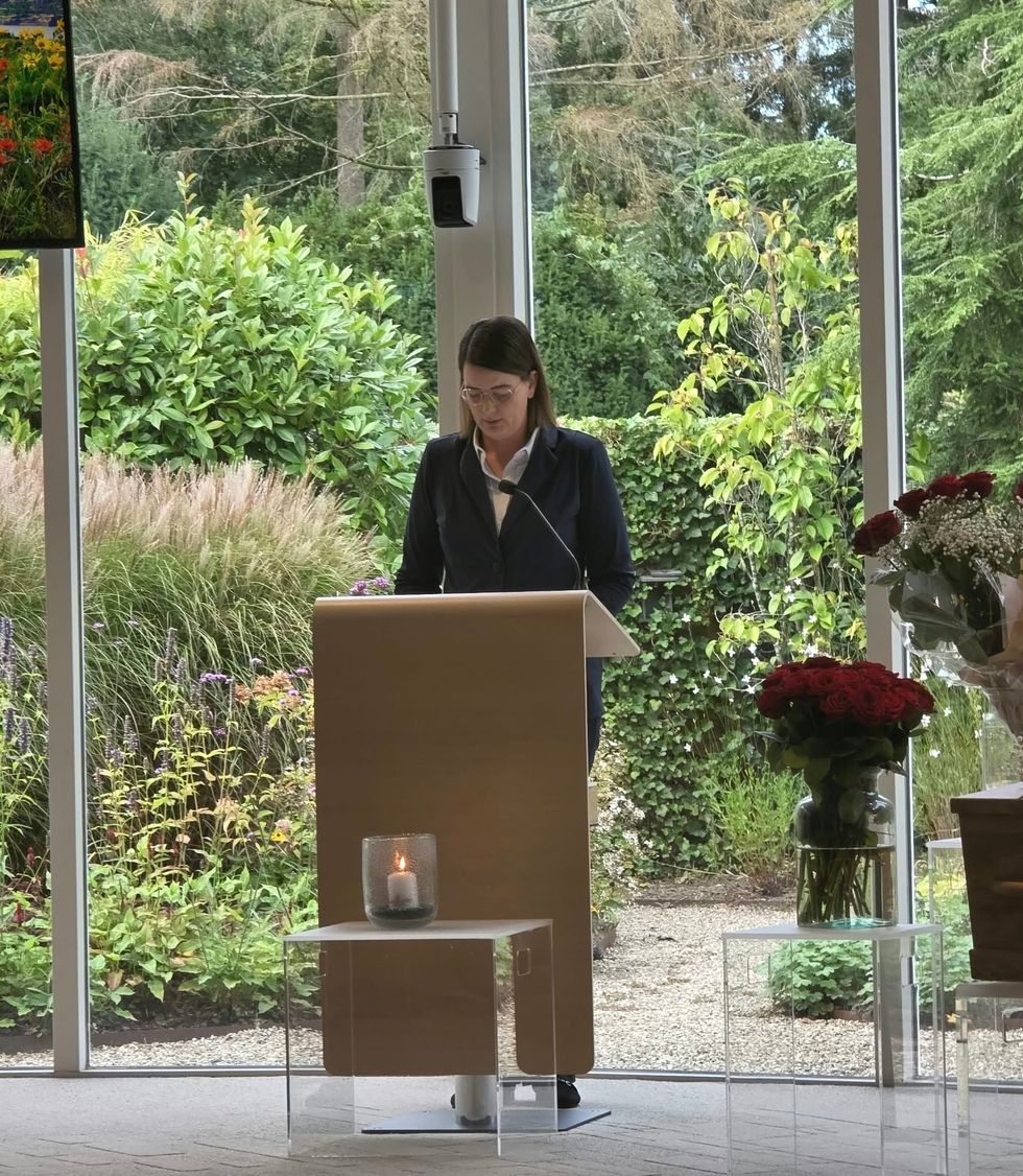 Portret van een vrouw in een grijze blazer die buiten staat met kale bomen en een logo in de hoek.