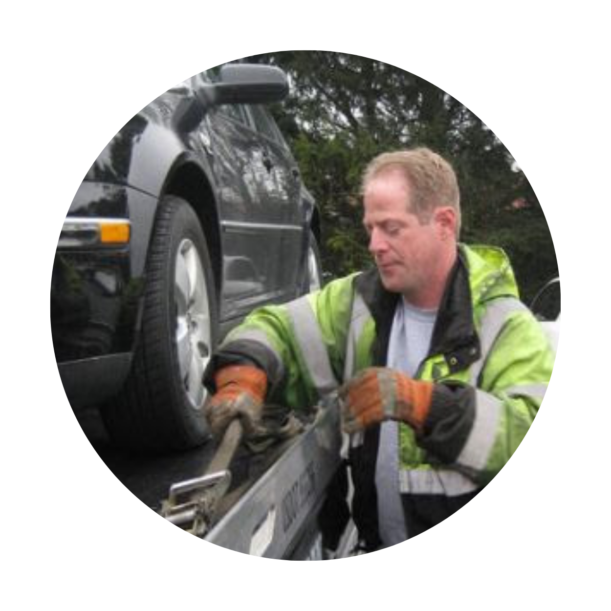 Tow truck operator securing a black car with orange gloves and green safety jacket.