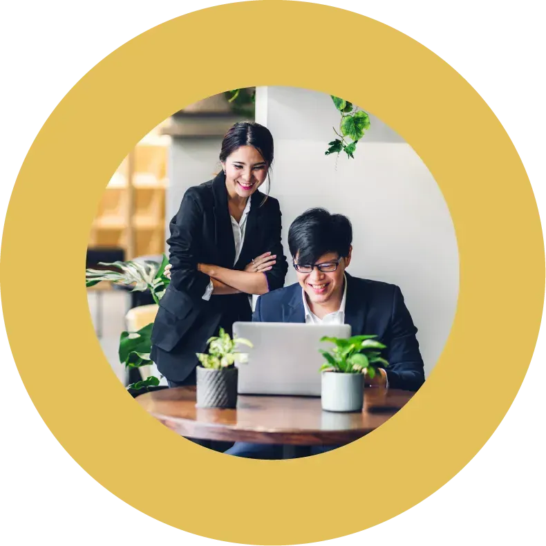 Two office workers looking at a laptop at work surrounded by plants