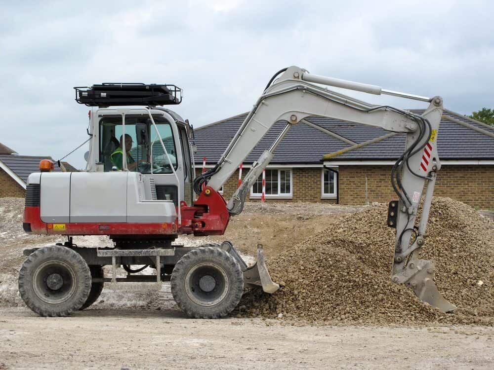 A White and Red Excavator is Moving Dirt on a Construction Site — Matt's Mini Machines in Palmwoods, QLD