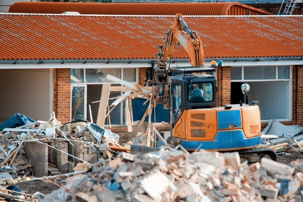 A Bulldozer is Demolishing a Building With a Pile of Rubble in Front of It — Matt's Mini Machines in Rosemount, QLD