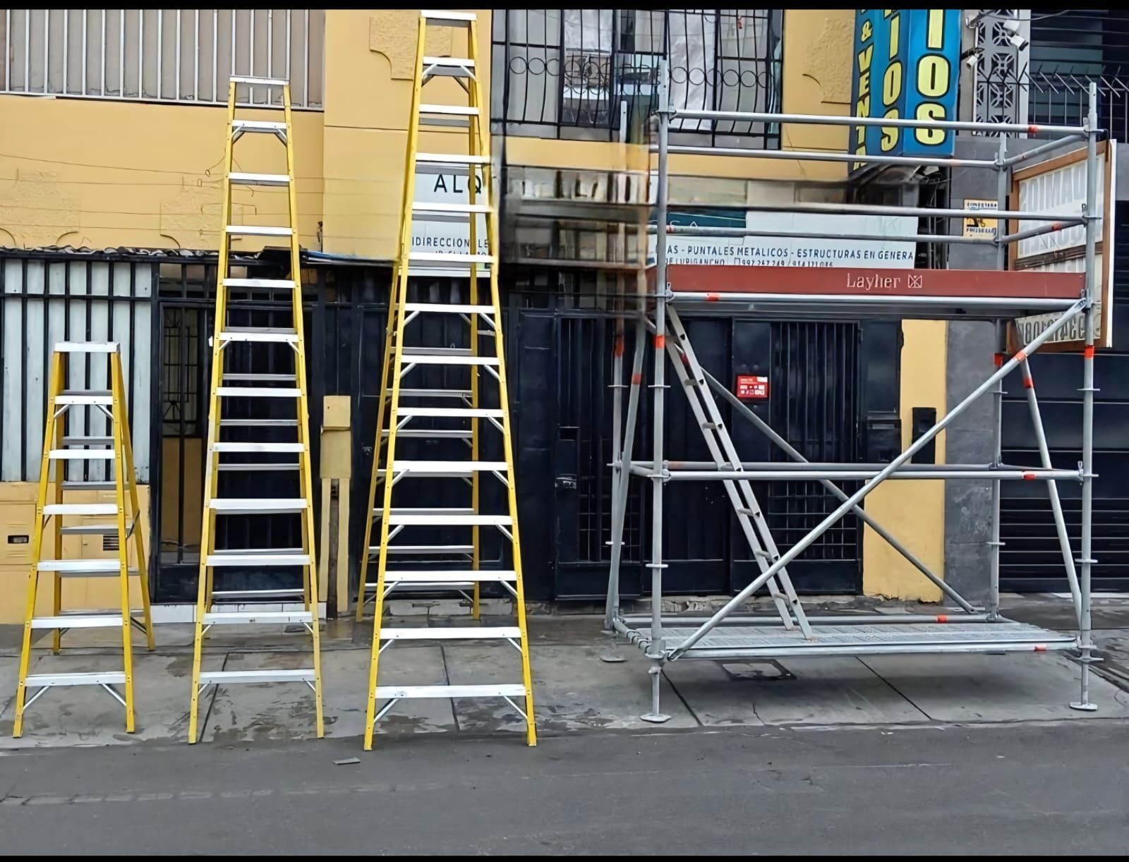 Andamios y escaleras en el exterior de la fachada de un edificio, con barreras de seguridad amarillas y grises.