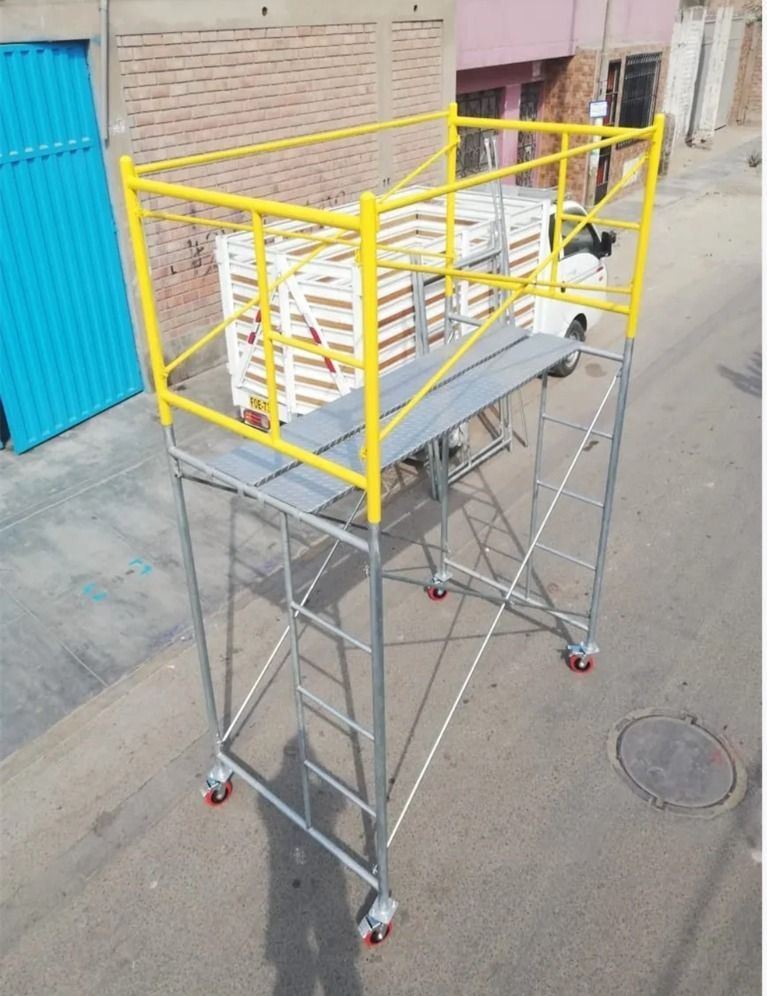 Carro de plataforma de metal amarillo con barandillas y cuatro ruedas giratorias en una calle junto a un edificio.