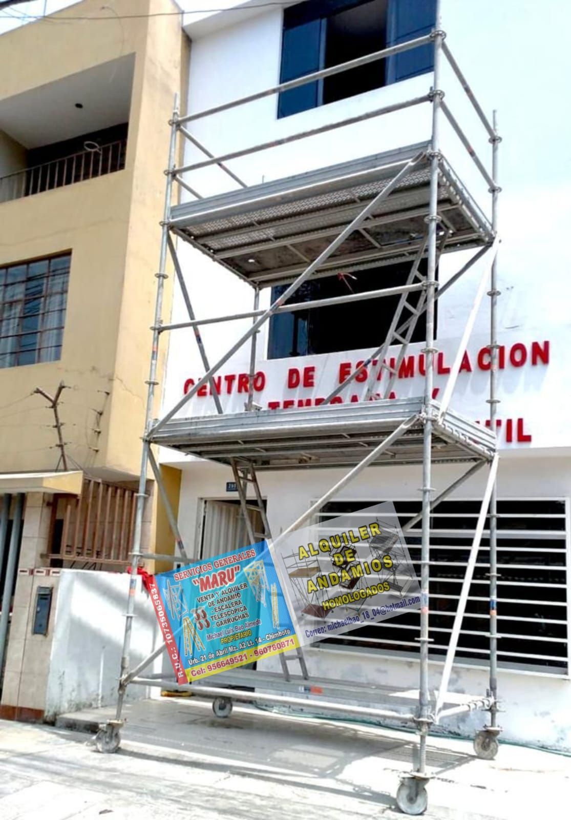 Andamio metálico frente a un edificio beige con letreros rojos en español y una colorida pancarta debajo.